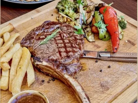 Prime rib eye steak on a wooden board with chips and grilled vegetables at Sirtaki Tavern